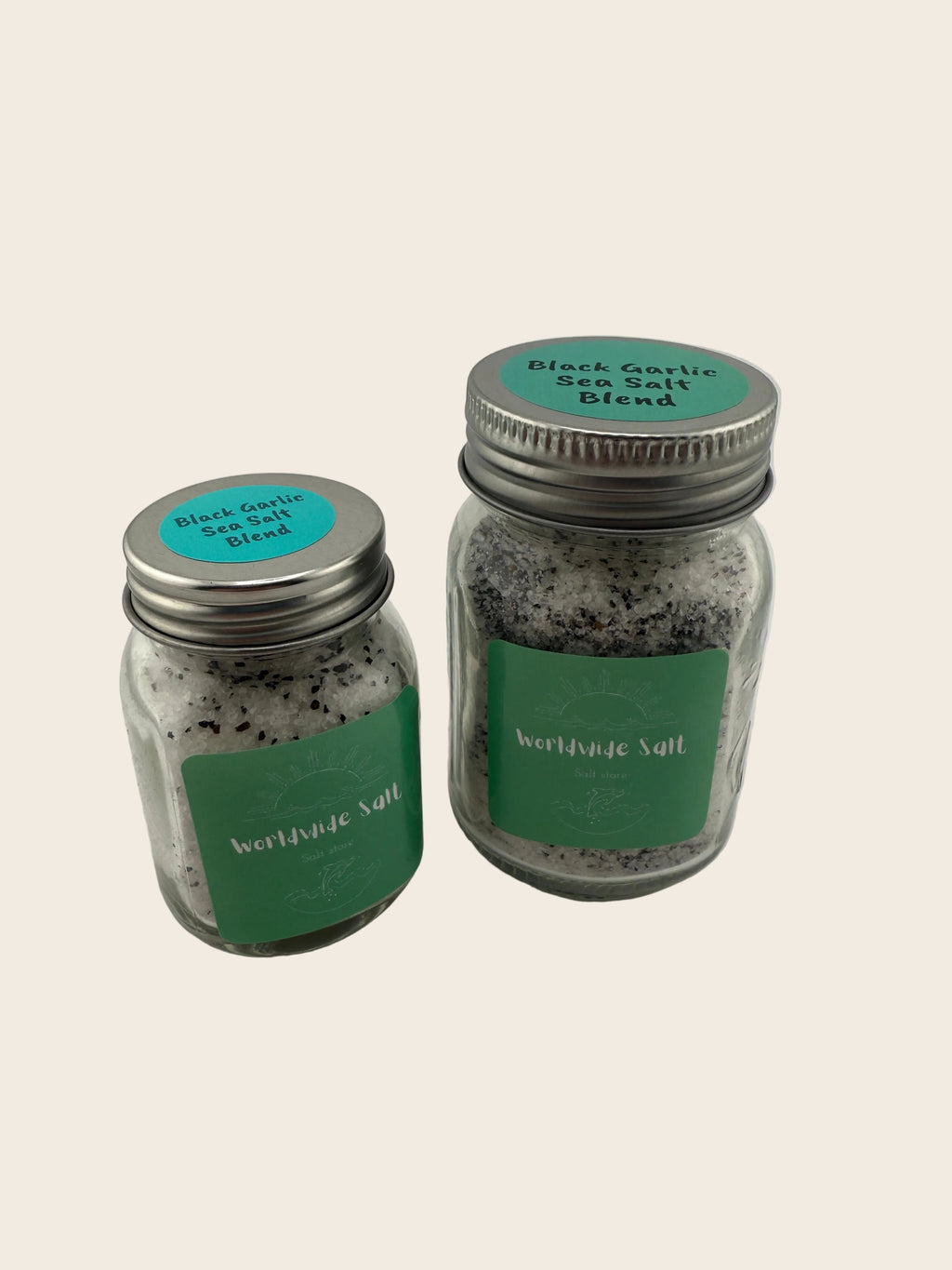 Two jars of black garlic salt blend with green labels on a white background