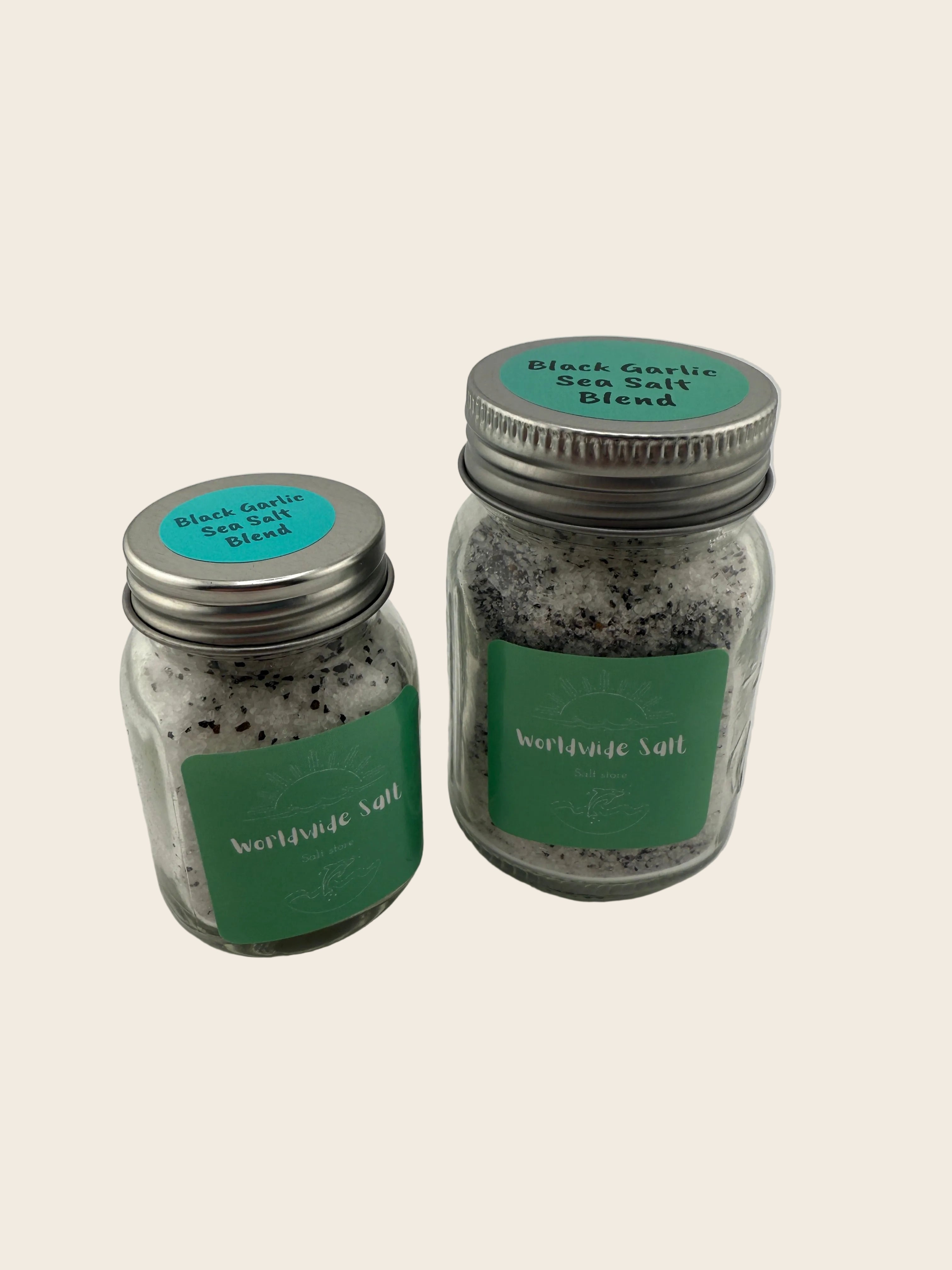 Two jars of black garlic salt blend with green labels on a white background