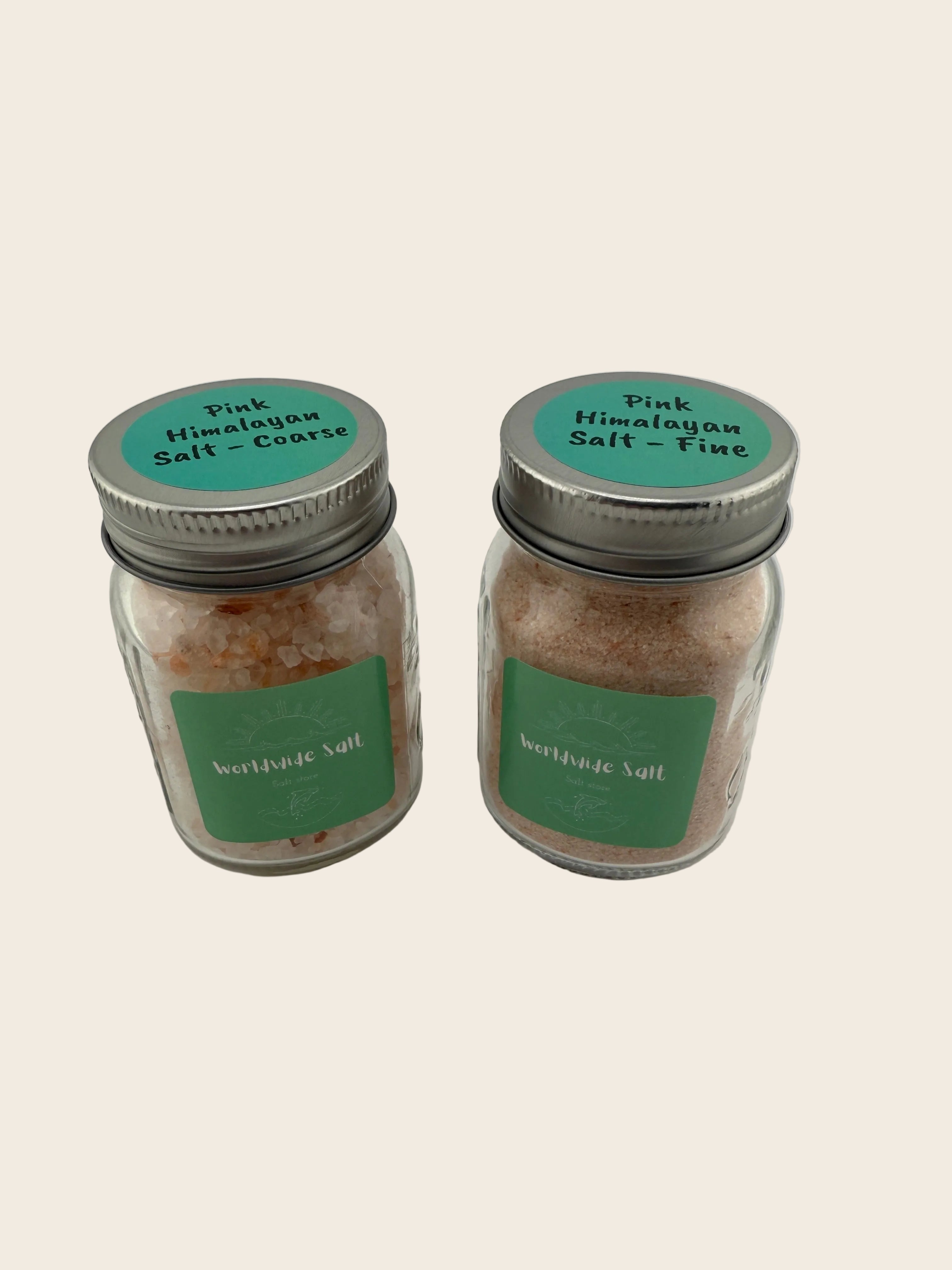 Two jars of pink Himalayan salt with green labels on a light gray background