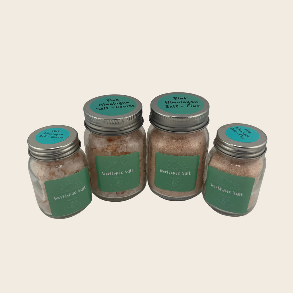 Four jars of pink Himalayan salt with green labels on a gray background